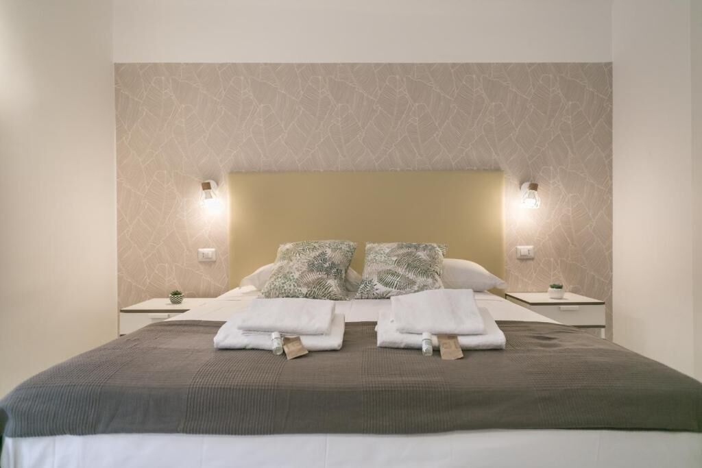 Una cama bien hecha con dos almohadas, una mesita de noche con lámpara y una pared con textura.