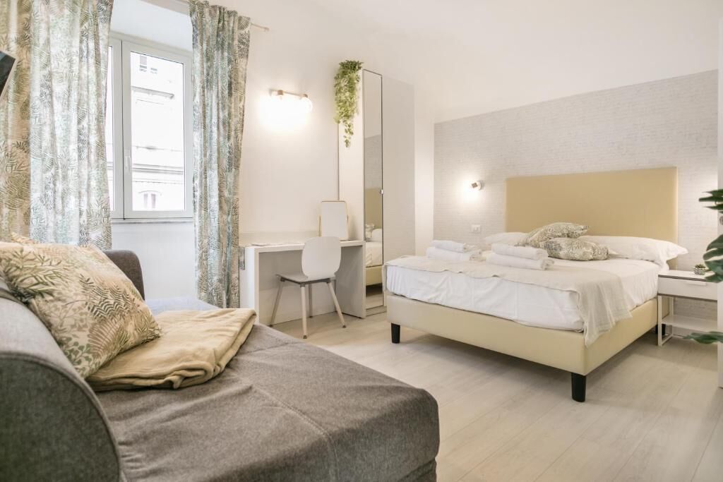 A bedroom with a bed, a desk, a chair, and a sofa.