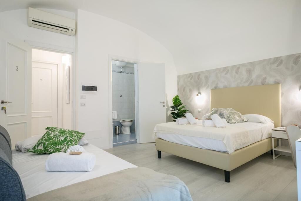 Una habitación de hotel moderna con una cama grande, una mesita de noche y una zona de ducha visible a través de una puerta abierta.