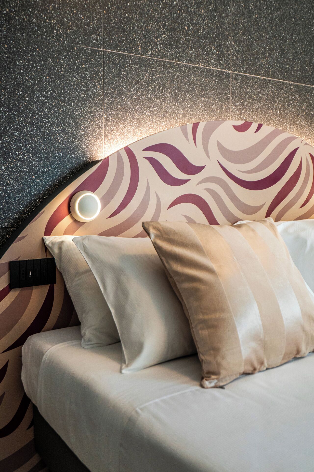 Ein Bett mit Kopfteil mit Wellenmuster, zwei Kissen und ein Nachttisch mit Lampe.