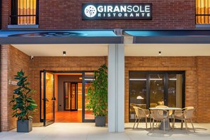 Exterior del restaurante Giransole, con fachada de ladrillo, zona de mesas al aire libre y puertas de entrada.