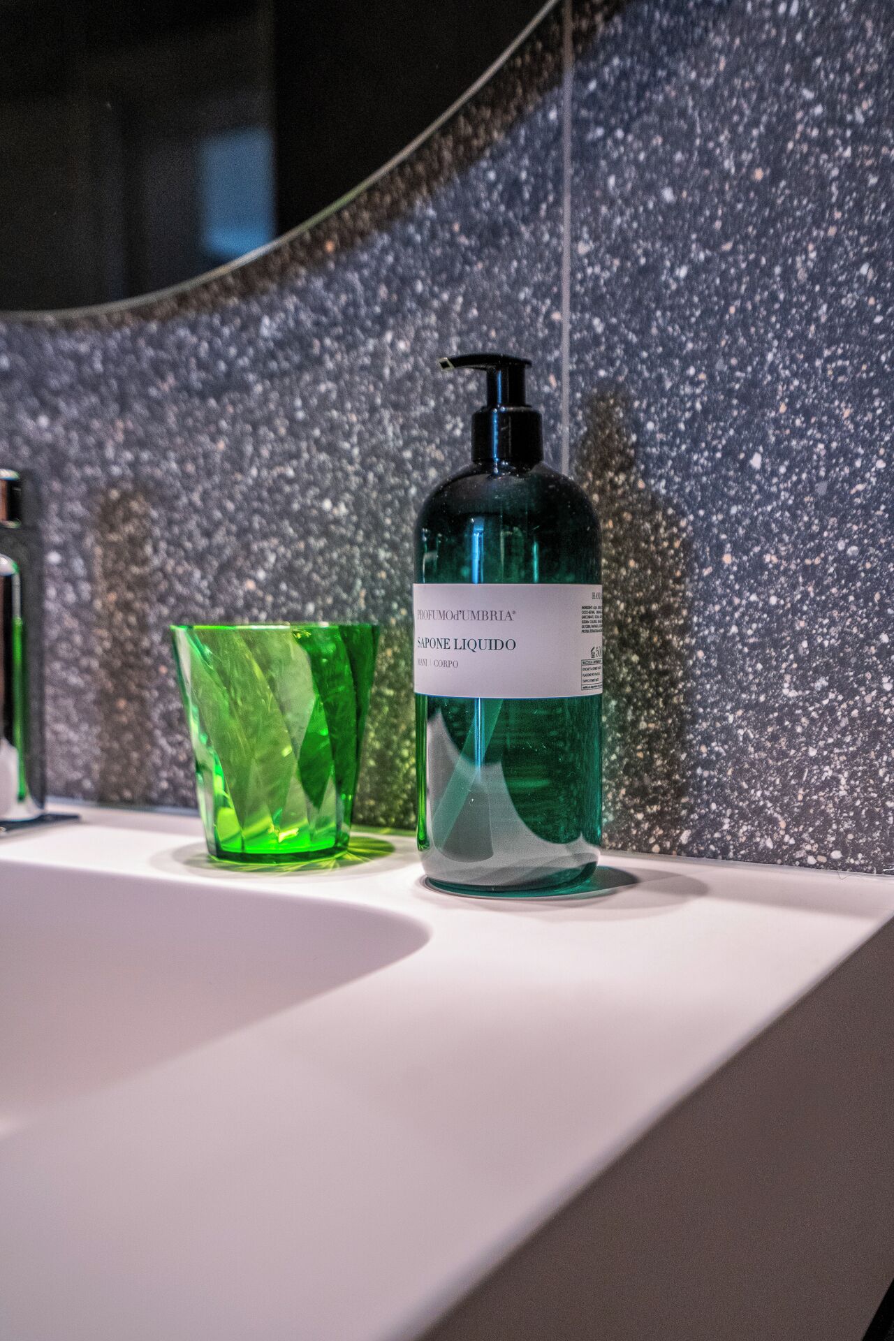 A bathroom with a white sink, a green glass, and a bottle of soap.