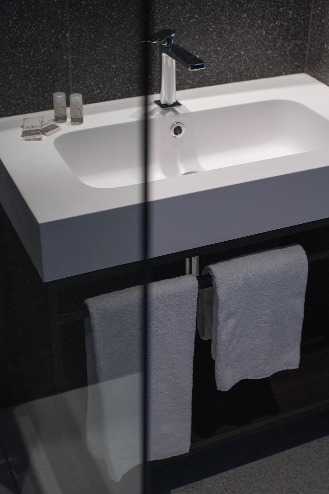 Ein modernes Badezimmer mit einem weißen Waschbecken, einem schwarzen Wasserhahn und zwei weißen Handtüchern an einem Handtuchhalter.