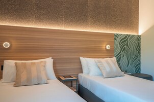 Habitación de hotel con dos camas, cabecero de madera y pared con estampado verde.