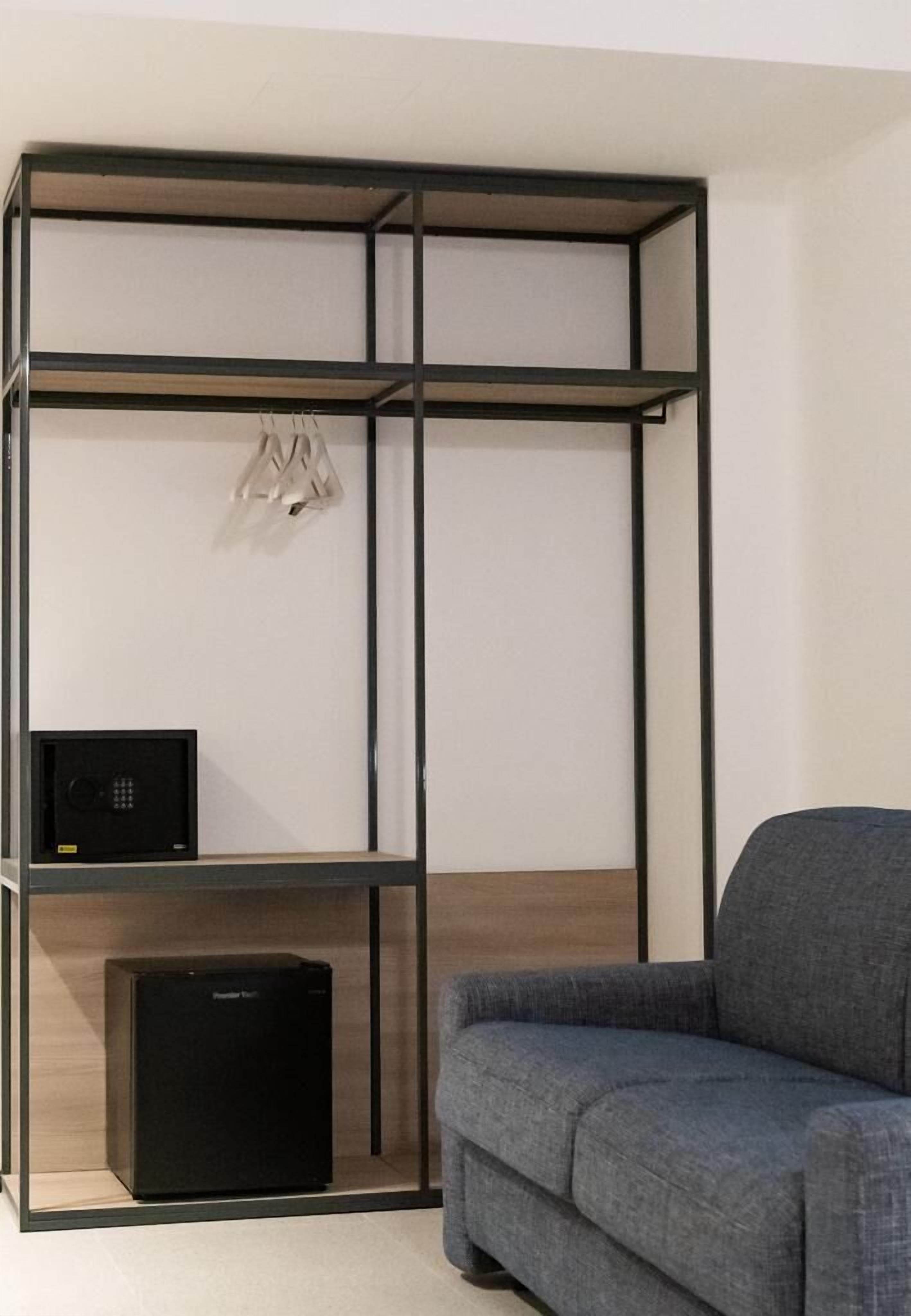 A room with a grey sofa, a black storage unit with a microwave, and a hanging coat rack.