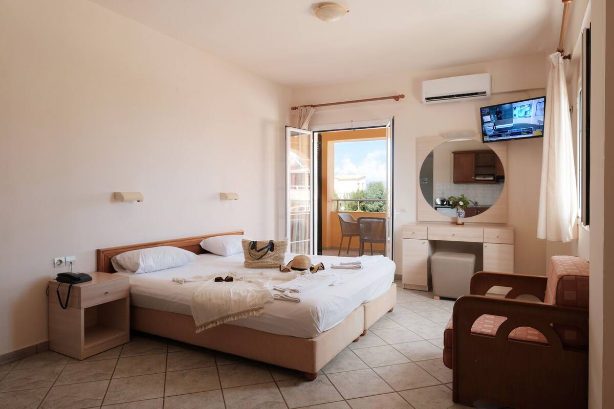 A hotel room with a bed, bedside table, TV, and a view of the outdoors.
