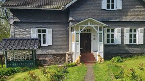 A two-story house with a dark grey exterior, white shutters, and a small porch with steps leading to the front door. - Dreamholiday - Stylish large vacation home with garden for 20+ people (Mittelhof)