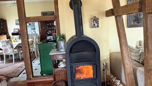 A room with a wood-burning stove, wooden beams, a green cabinet, and a dining area in the background. - Dreamholiday - Stylish large vacation home with garden for 20+ people (Mittelhof)