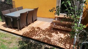 Uma área de pátio com mesa e cadeiras, um deck de madeira e uma pequena planta.
