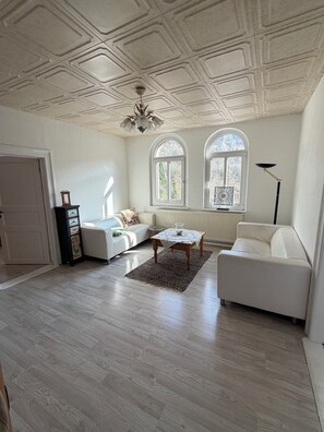 Amplia sala de estar con techo alto, dos ventanas de arco, un sofá blanco, una mesa de centro y una lámpara de pie.