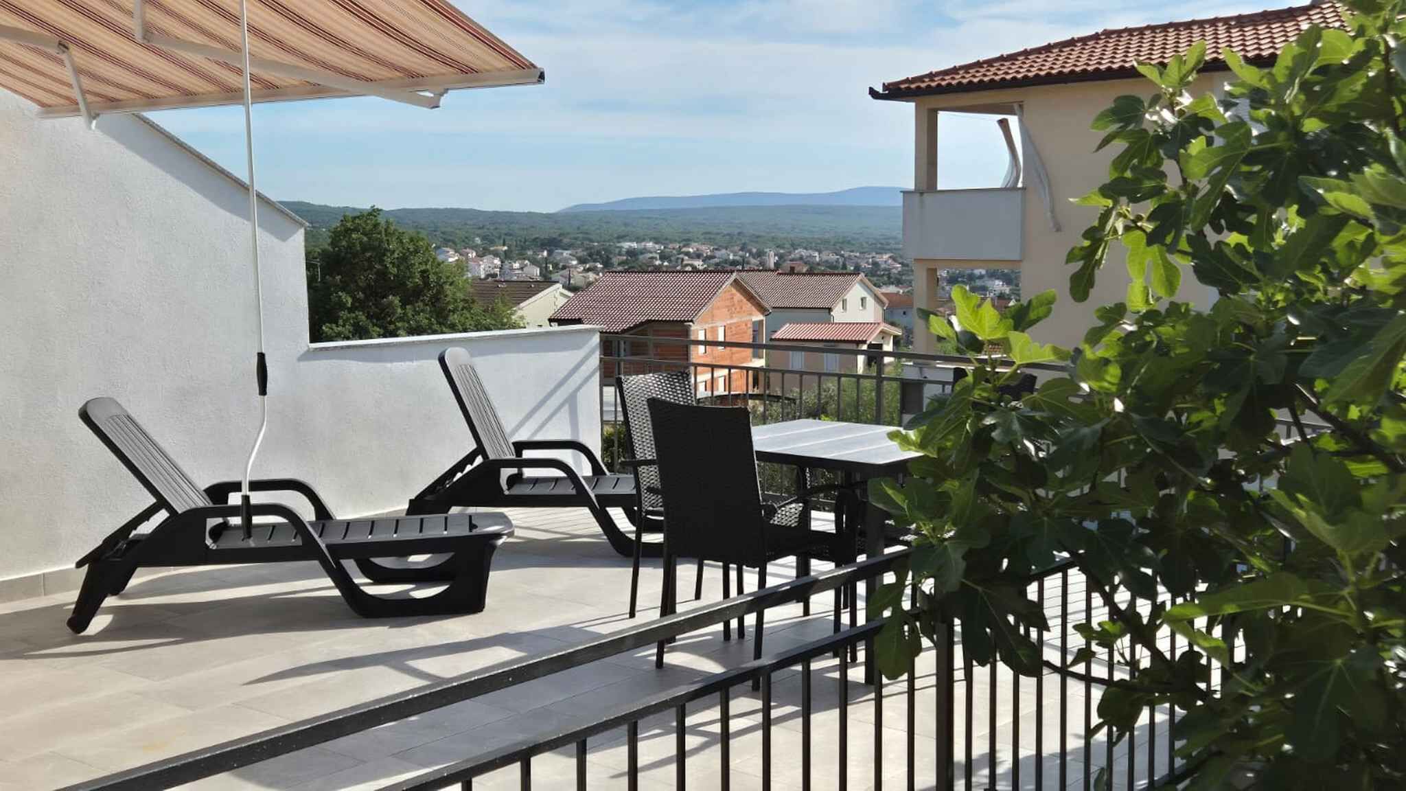Een balkon met een tafel en stoelen, uitzicht op een stad en een gebouw met een rood dak.