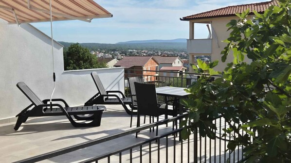 Ein Balkon mit Tisch und Stühlen, Blick auf eine Stadt und ein Gebäude mit rotem Dach.