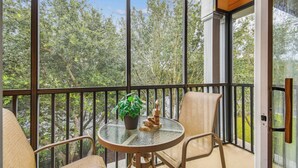 A balcony with a glass table, two chairs, a potted plant, and a decorative sculpture. - 3BR Condo at Bahama Bay Resort (Davenport)