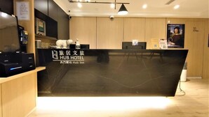 A hotel reception desk with a black counter, a clock, a phone, and a poster on the wall. - HUB HOTEL XIMEN XINING INN (Taipei)