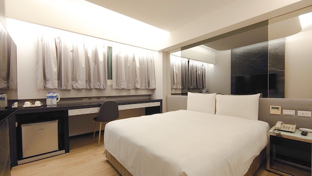 A hotel room with a large bed, a desk with a chair, a small desk, a mirror, and a telephone. - HUB HOTEL XIMEN XINING INN (Taipei)