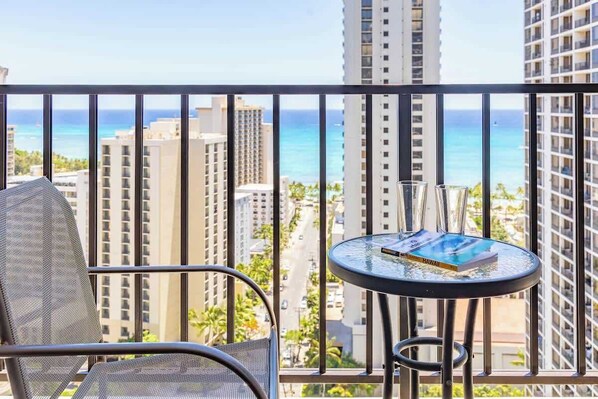Un balcone con una sedia e un tavolino, affacciato su una vista della città e dell'oceano.