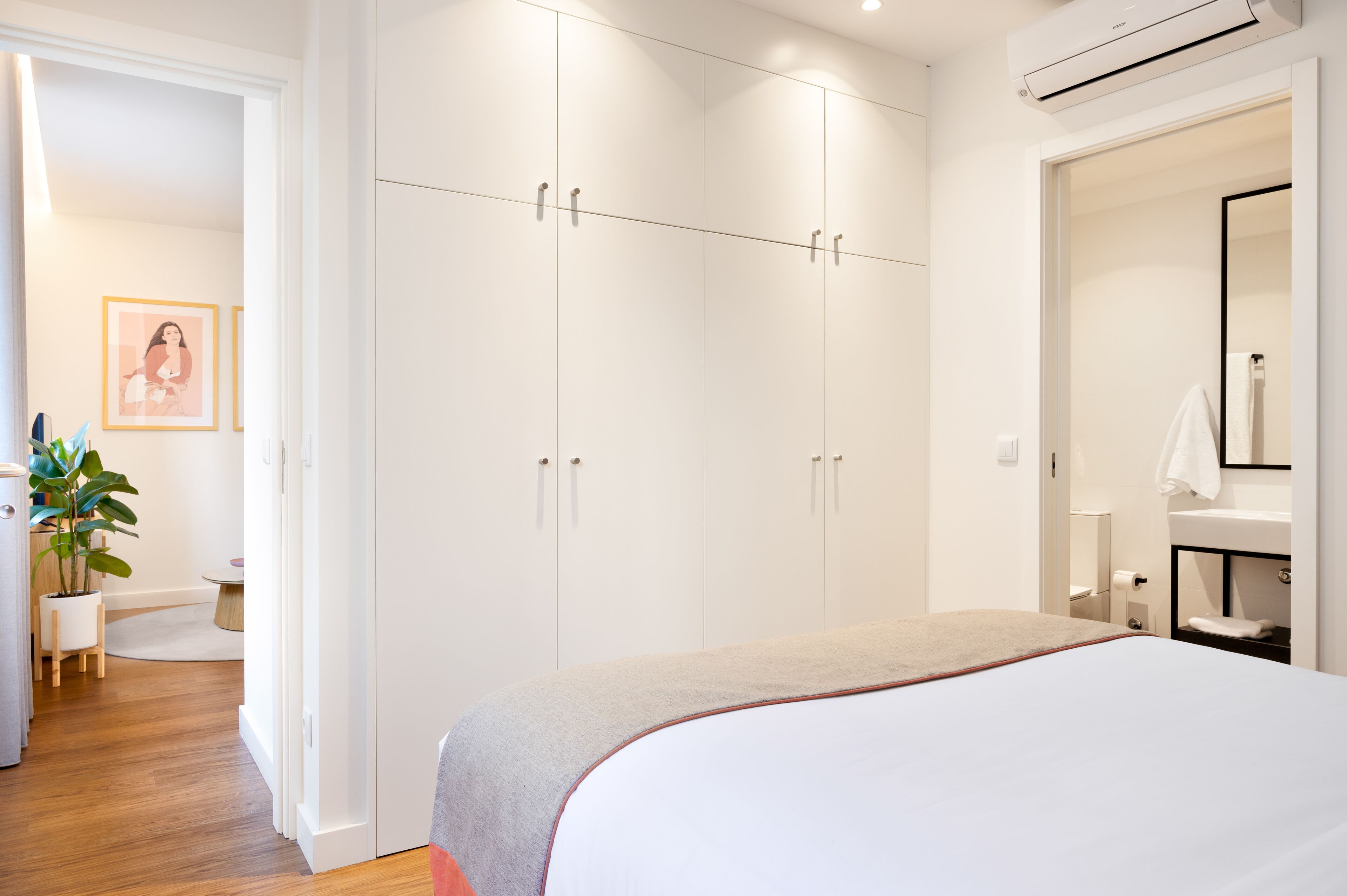 A bedroom with a bed, a wardrobe, a bathroom with a sink and mirror, and a potted plant.