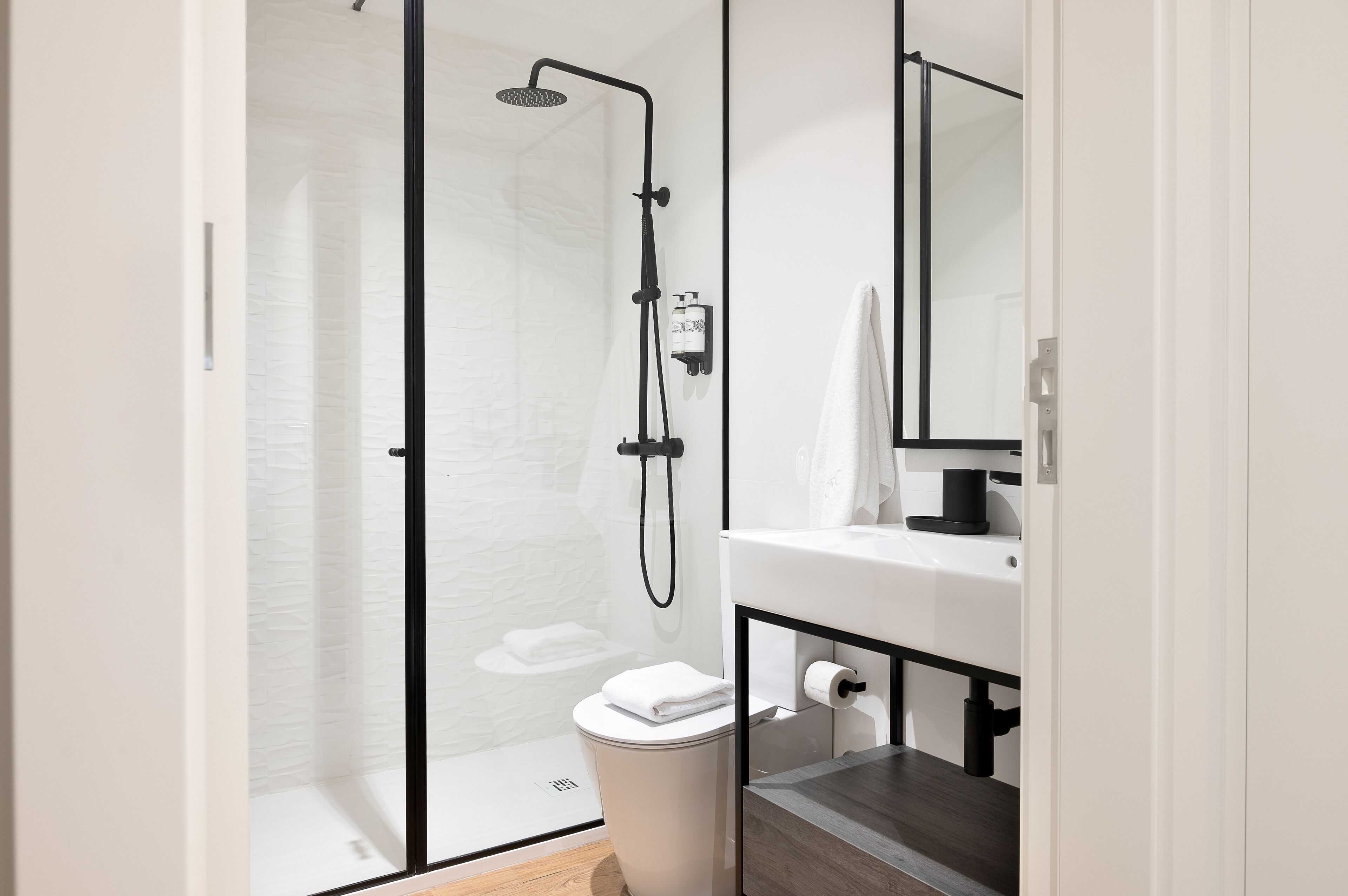A modern bathroom with a glass-enclosed shower, a white sink, and a mirror.