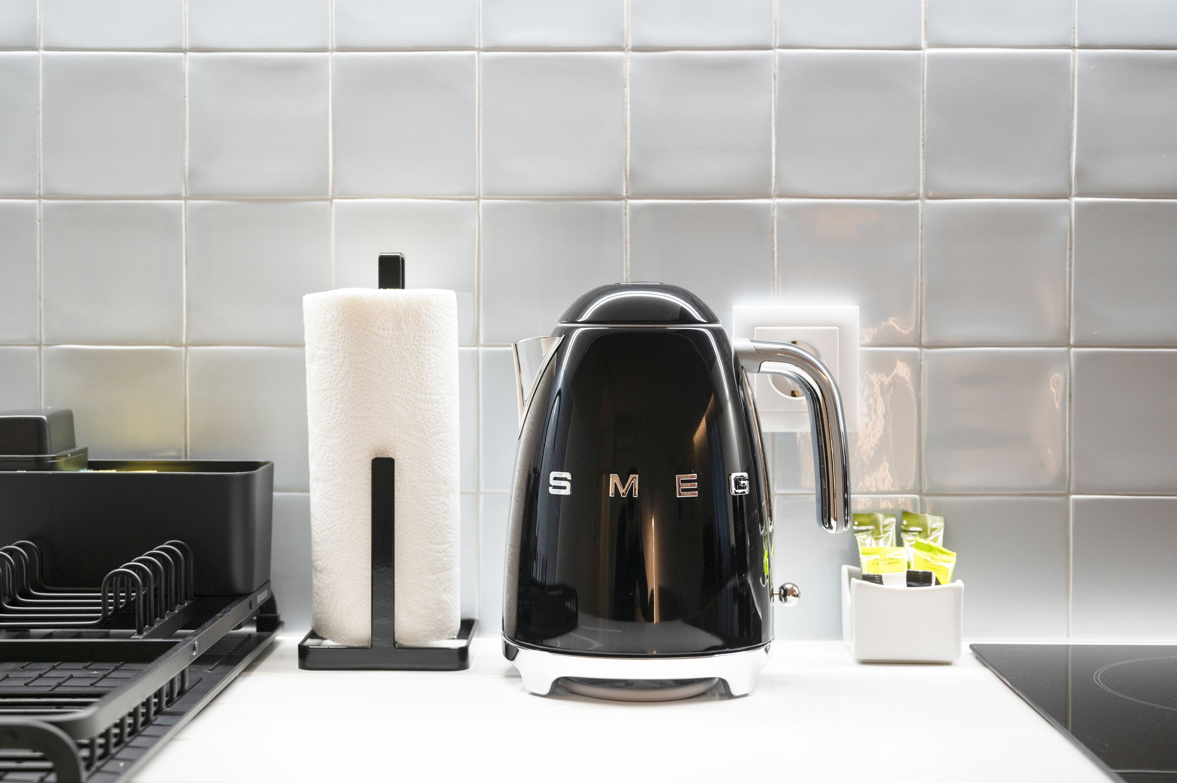 A kitchen with a black coffee maker, a white paper towel holder, and a white container with yellow packets.