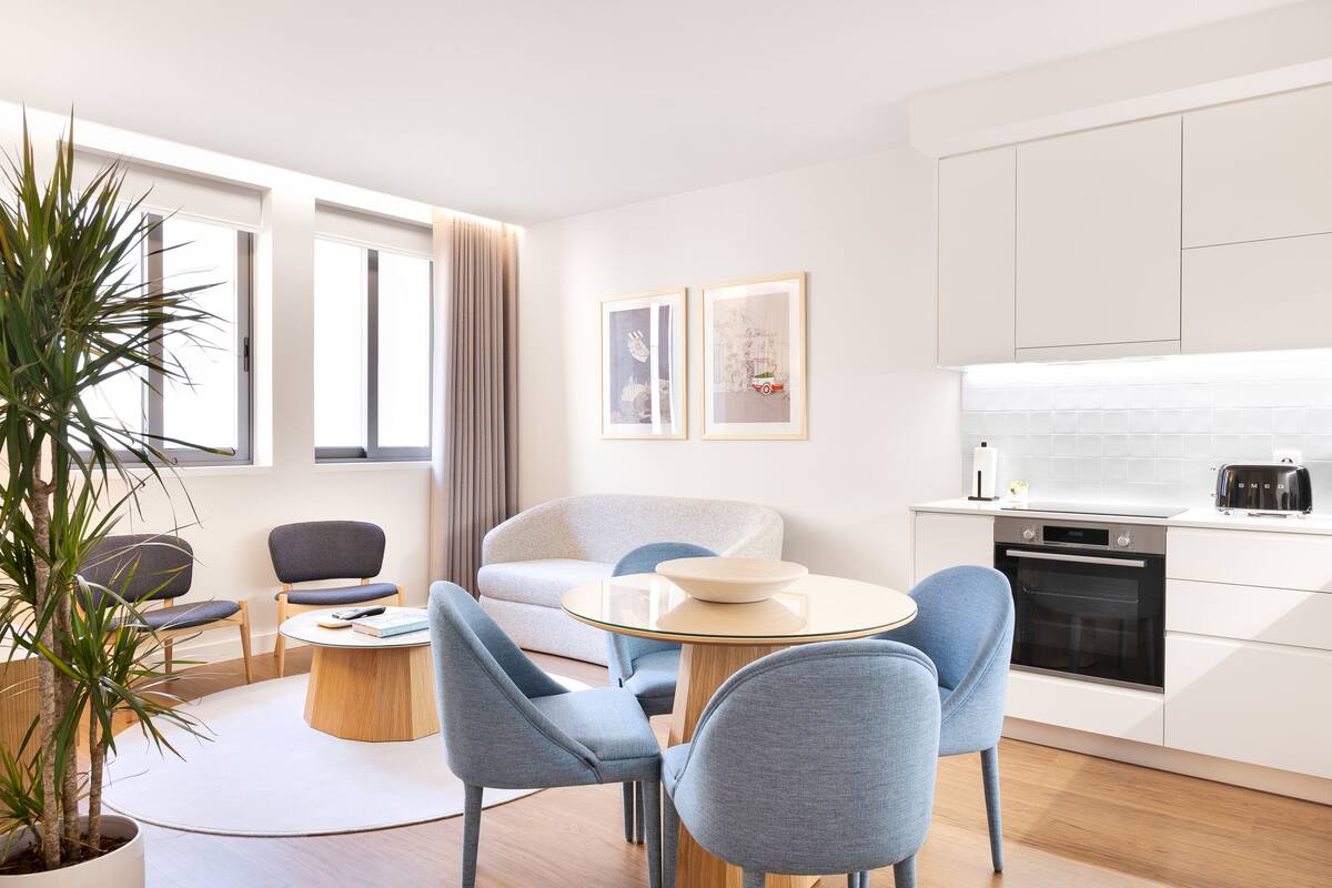Een moderne woonkamer met een ronde glazen tafel, blauwe stoelen, een grijze bank en een potplant.