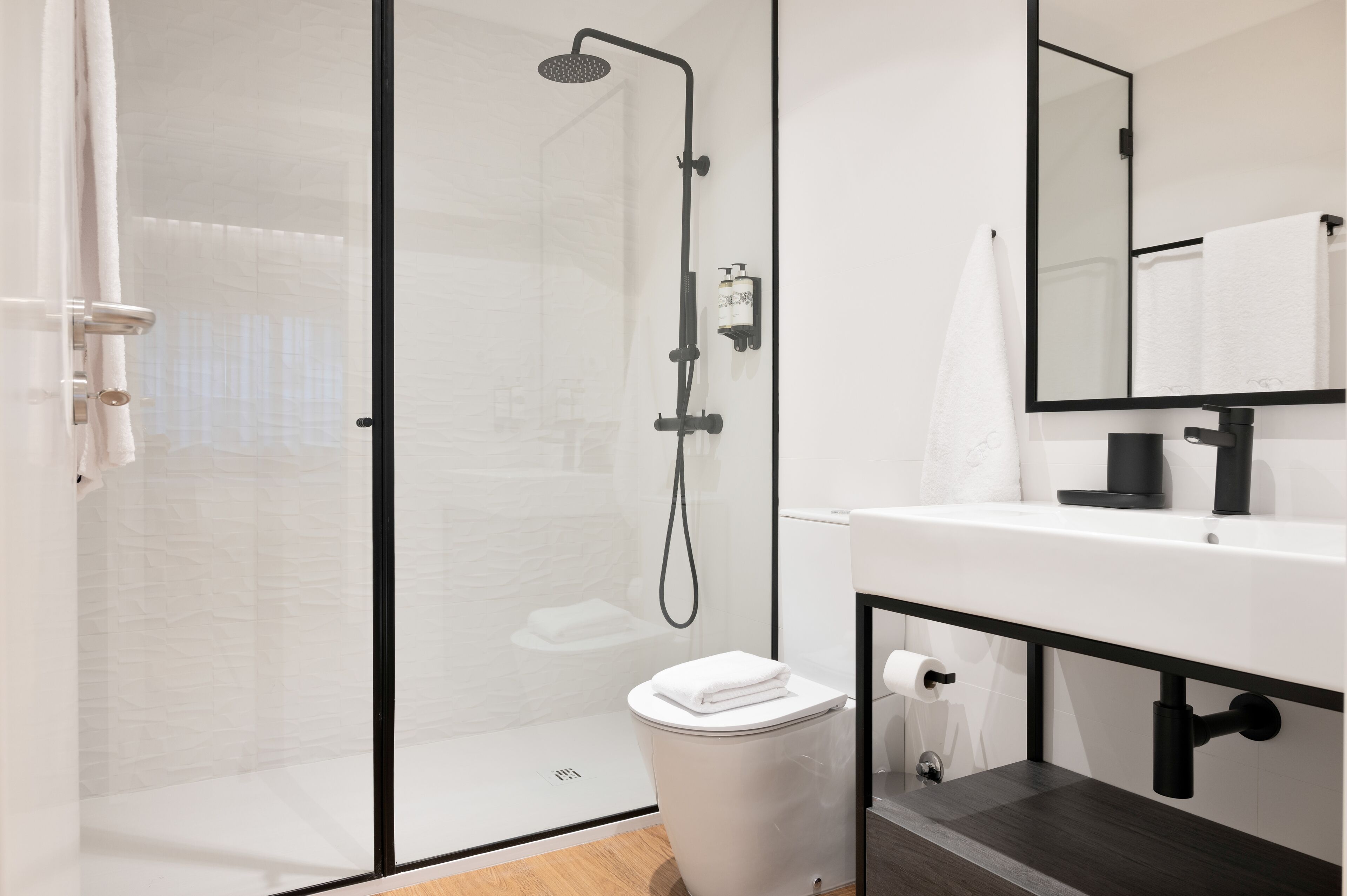Une salle de bain moderne avec une douche à parois de verre, un lavabo blanc et un miroir au-dessus du lavabo.