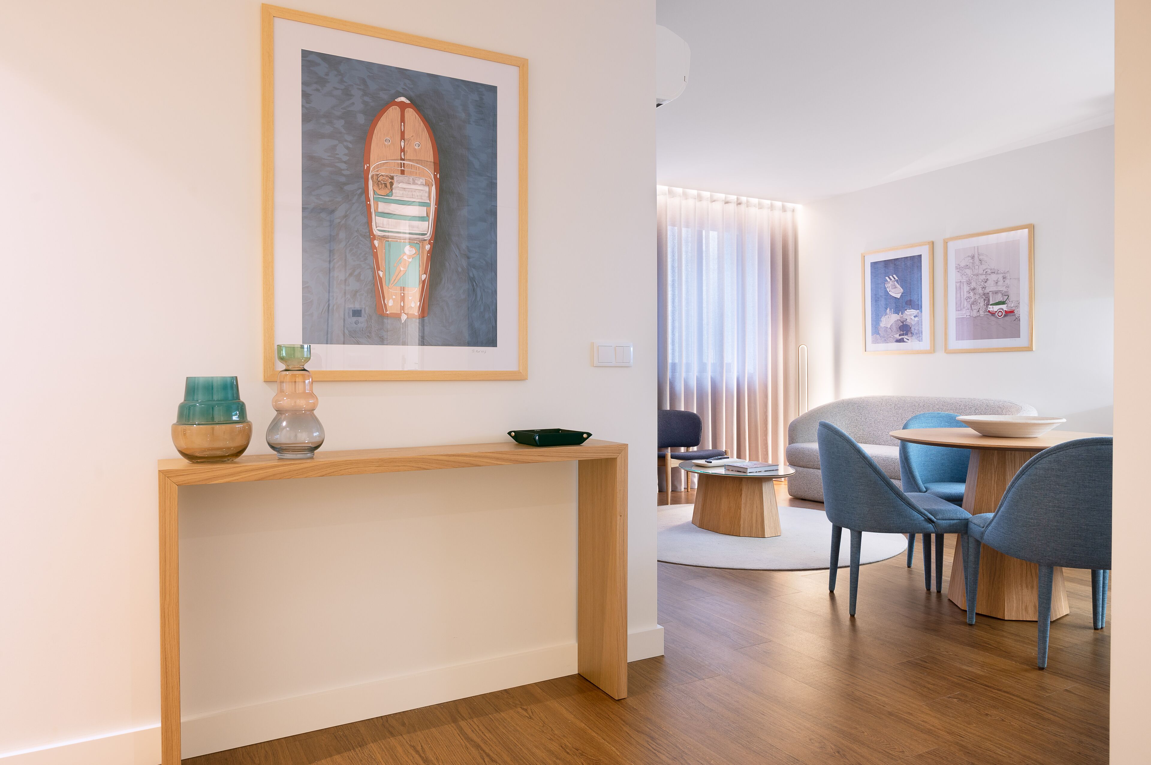 A modern living room with a wooden console table, a round coffee table, and a seating area with blue chairs.
