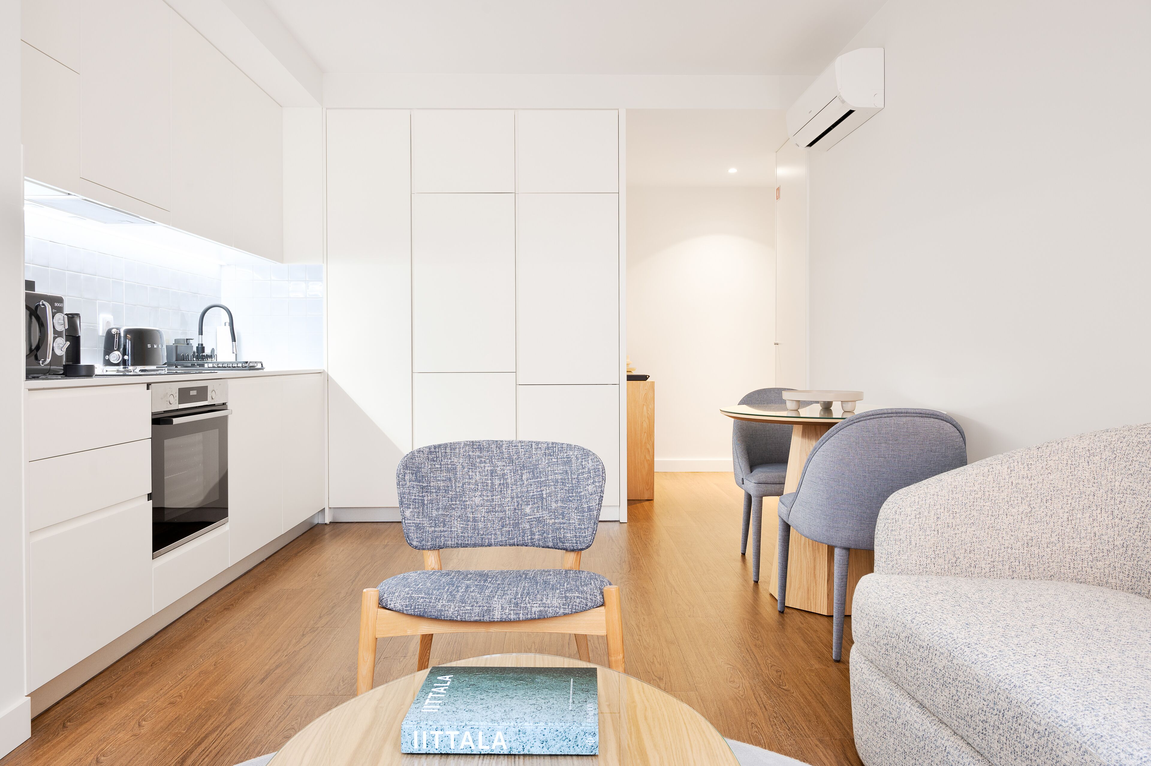 A modern kitchen with white cabinets, a built-in oven, and a dining area with a round table and two chairs.