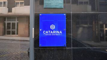 A building facade with two signs: one for 'IMPACTO CAPITAL Real Estate' and another for 'CATARINA Serviced Apartments'.