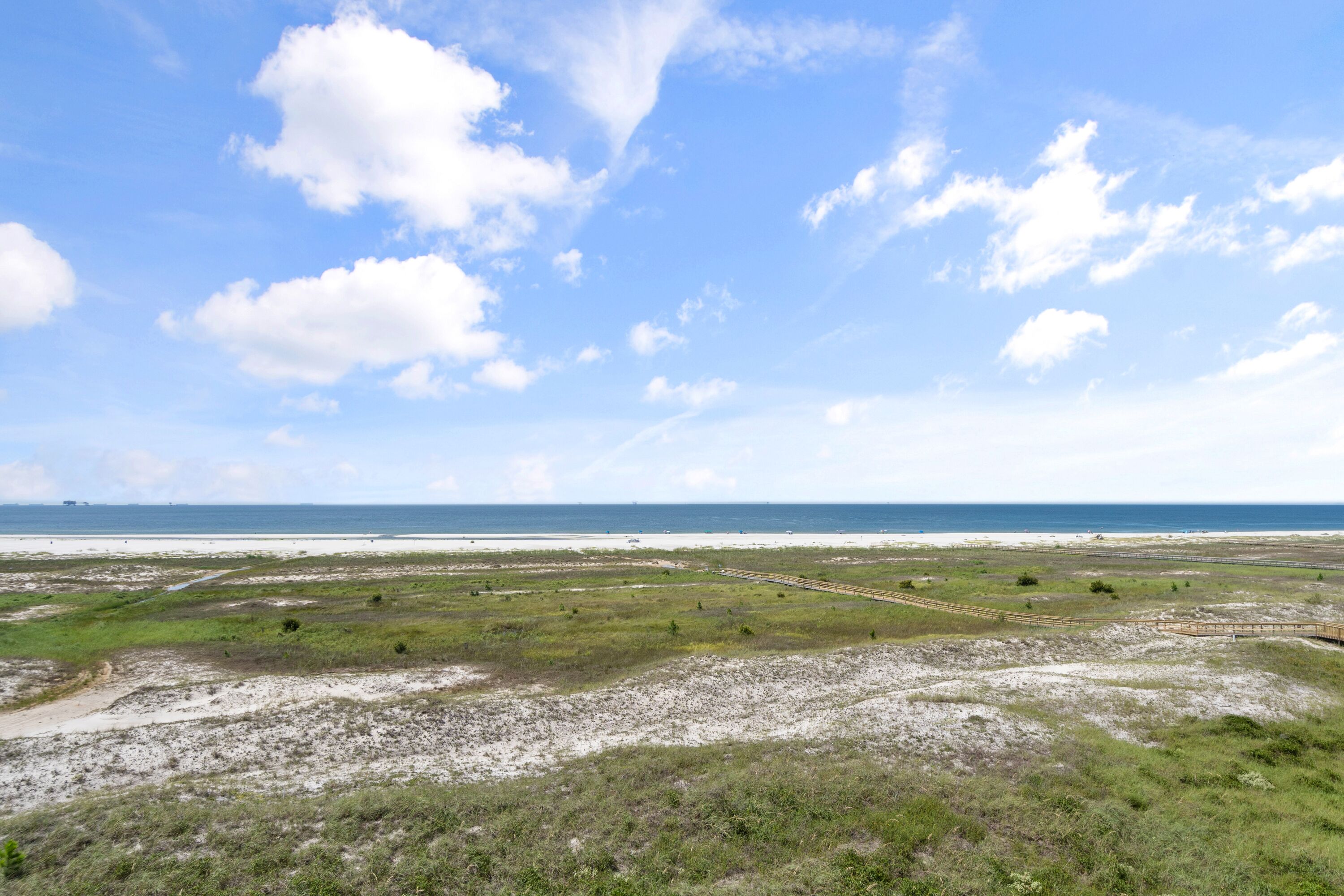 A coastal landscape with a sandy beach, grassy areas, and a clear blue sky.
