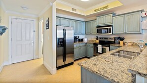 Una cucina con mobili azzurri, elettrodomestici in acciaio inossidabile, un piano di lavoro in granito e un cartello con la scritta 'WELCOME' appeso al soffitto.