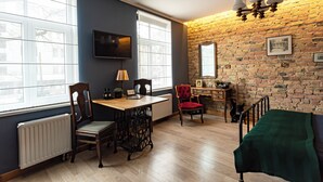 A room with a brick wall, a wooden table with chairs, a TV mounted on the wall, and a window with blinds. - Vintage Apartments BLACK / Free parking (Riga)