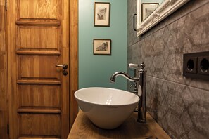Una puerta de madera, un lavamanos blanco con un grifo moderno y dos cuadros en la pared.