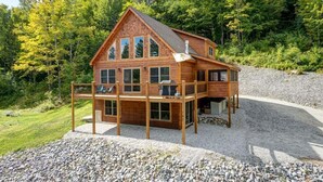 En træhytte med balkon, omgivet af træer og grus.