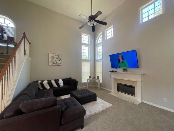 A living room with a sectional sofa, ottomans, a fireplace, a television, and a ceiling fan.