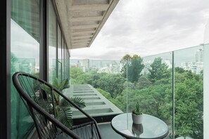 En balkon med gelænder af glas, et rundt bord og en potteplante.