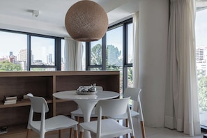 Un comedor moderno con una mesa redonda, sillas blancas, una lámpara colgante de fibras naturales y vistas a la ciudad a través de amplios ventanales.