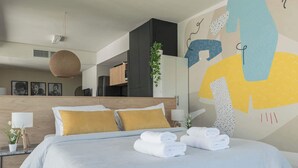 Et moderne hotelværelse med seng, et natbord, en vægmonteret lampe og en stor abstrakt vægdekoration.