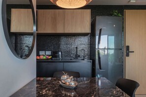 Eine moderne Küche mit schwarzem Fliesenrückwand, Holzschränken, einem Edelstahlkühlschrank und einer Marmarbeitung mit Obstschale.