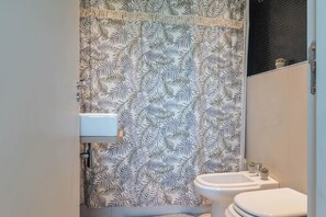A bathroom with a leaf-patterned shower curtain, a white sink, and a toilet.