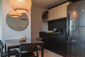 Eine moderne Küche mit einem schwarzen Kühlschrank, einer Mikrowelle und einem Holzkasten. Es gibt einen Esstisch mit Stühlen und einen runden Spiegel an der Wand.