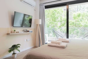 A modern hotel room with a large bed, a flat-screen TV, a balcony with a view of trees, and a small table with a chair. - MOT Rentals + Azcuenaga 1800 'B' - Loft in Recoleta Mall (Recoleta)