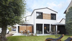 Une maison moderne à deux étages dotée d’un patio aménagé avec du mobilier d’extérieur et une pelouse.