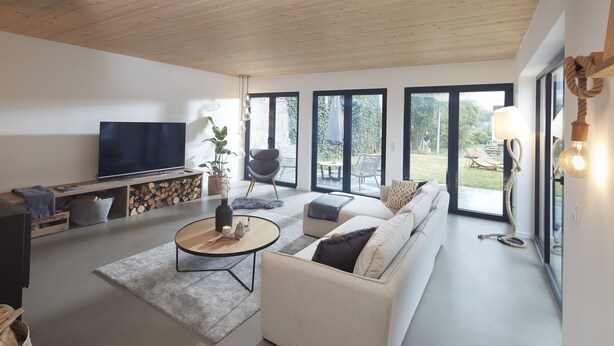 Un salon moderne avec un canapé, une table basse, un téléviseur et une vue sur l’extérieur.