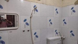 Ein Badezimmer mit weißen Fliesen und blumigen blauen Mustern, einer Toilette und einer Dusche mit Duschschlauch.