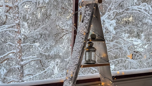 Escala metàl·lica amb un fanal i llums de cadena davant d'un paisatge nevós.