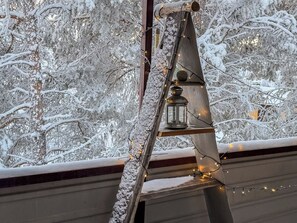 Een metalen ladder met een lantaarn en lichtjes, voor een besneeuwde achtergrond.