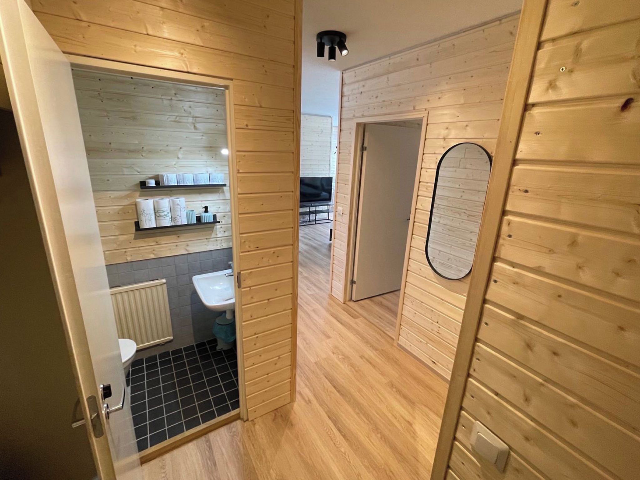 Un interior de madera con un baño, un estante con artículos de aseo y un espejo.