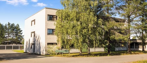 A modern two-story building with a flat roof and a large tree in front.