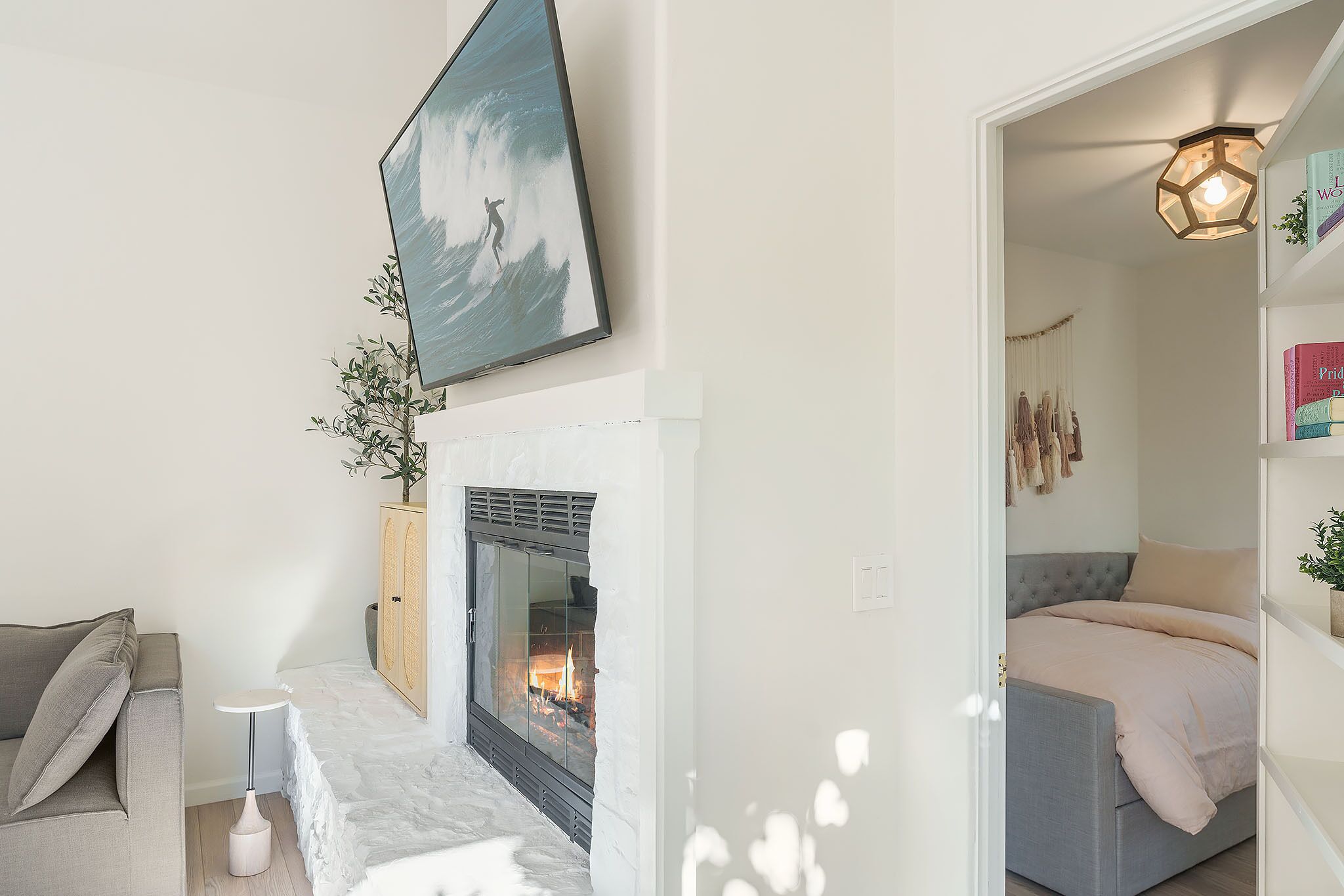 A modern living room with a fireplace, a sofa, and a bed in an adjacent room.