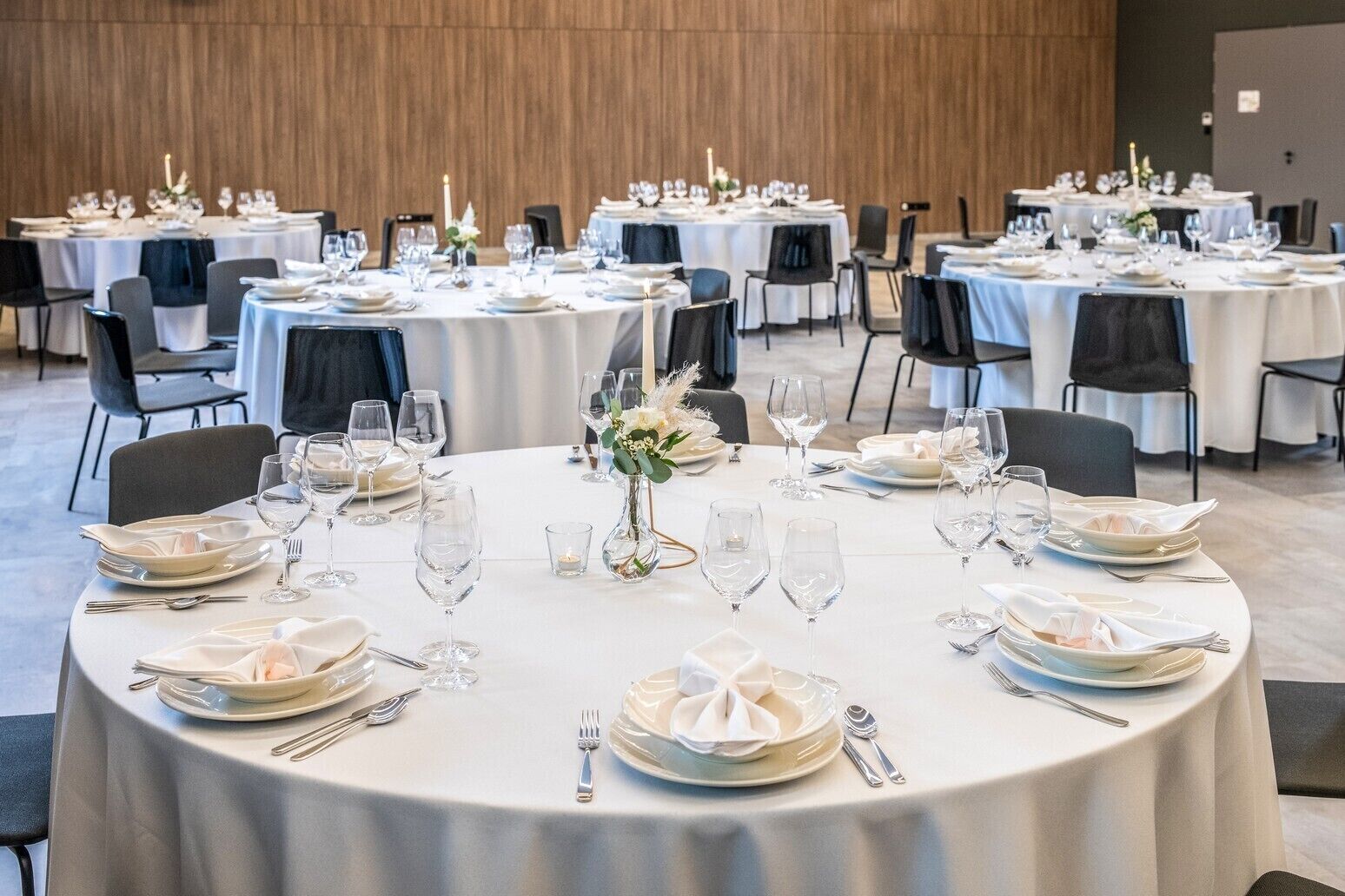 Un salón de banquetes con mesas redondas dispuestas para cenar, con manteles blancos y sillas negras.